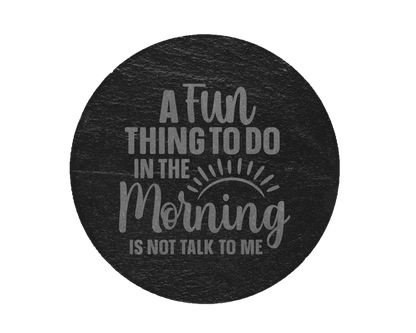 A laser engraved round slate coaster that says a fun thing to do in the morning is not talk to me